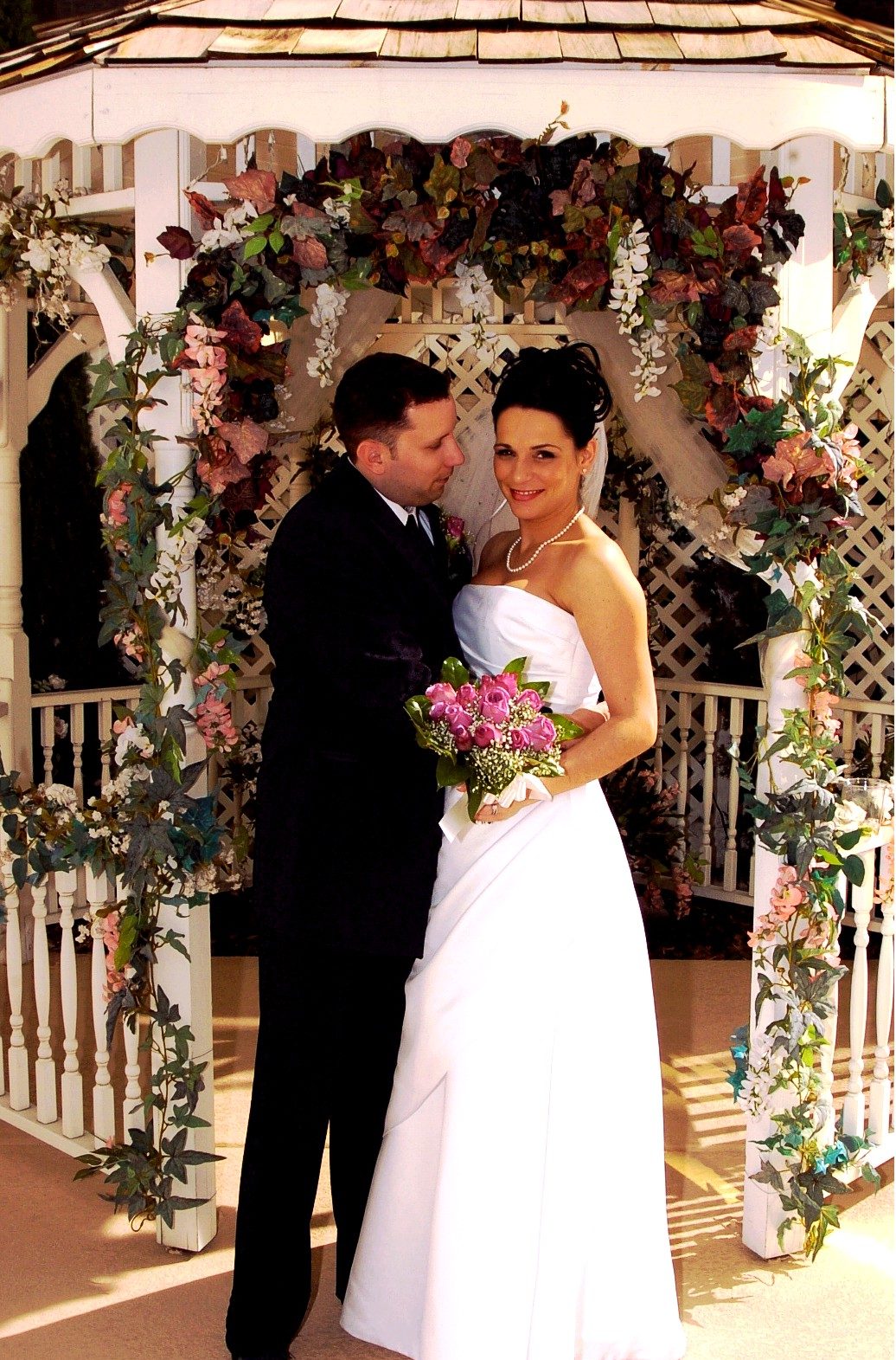 A couple standing in the flower-covered chapel gazebo